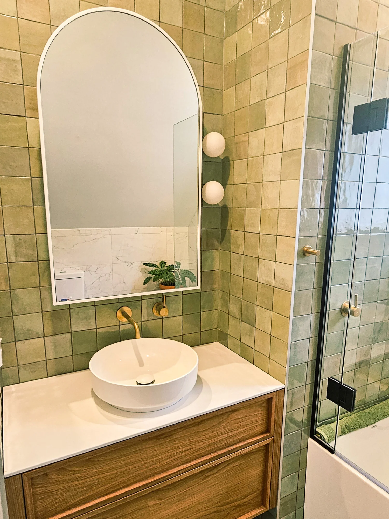 Bathroom with an arched mirror, green tiles and timber vanity